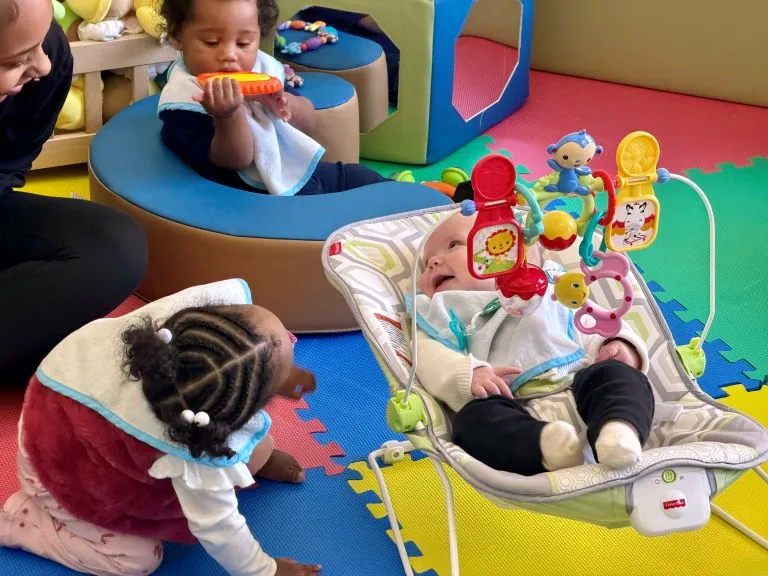 Two toddlers and a baby playing in a bright colorful room