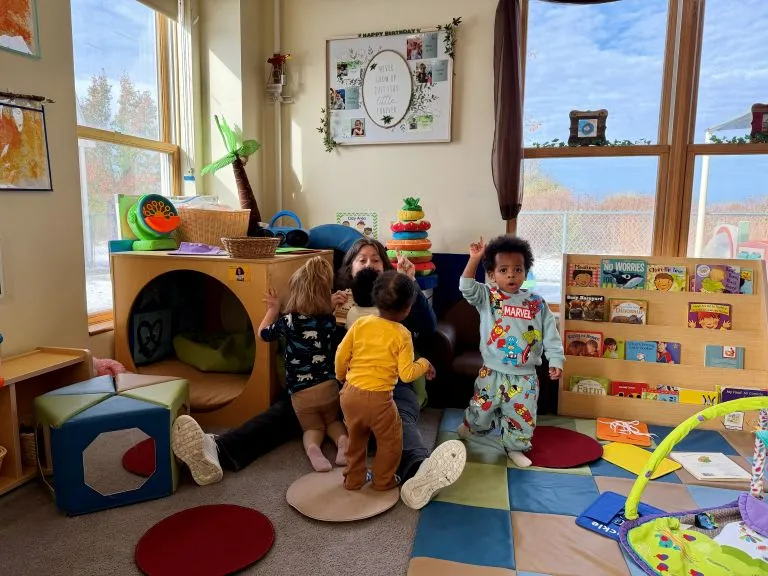 Teacher playing with four toddlers in a bright sunny classroom