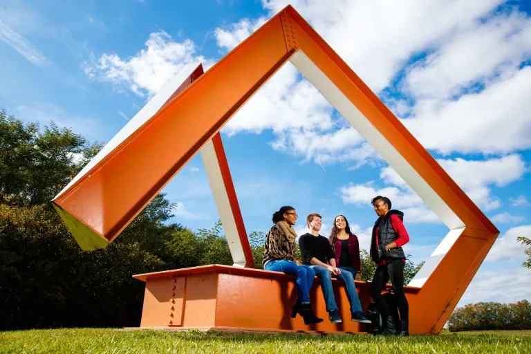 Students sitting on a sculpture and talking outside
