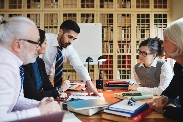 Image of five individuals sitting at a table with books, paper and pens