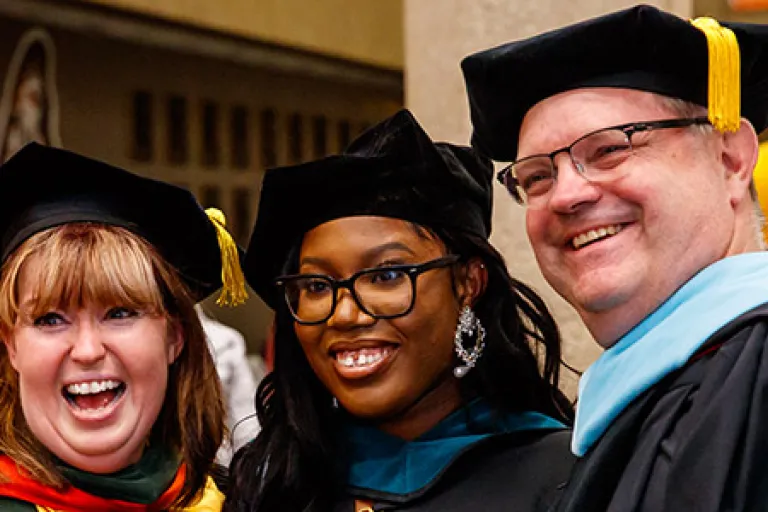 Image of three individuals in graduation regalia 