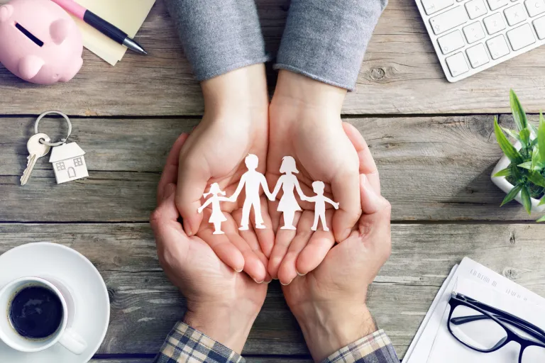 Image of table with cup, keys, keyboard, eyeglasses and two sets of hands holding a cutout of family