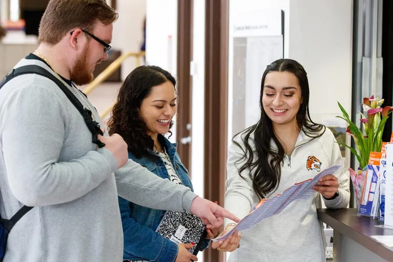 A woman shows a brochure to a couple in a campus setting.
