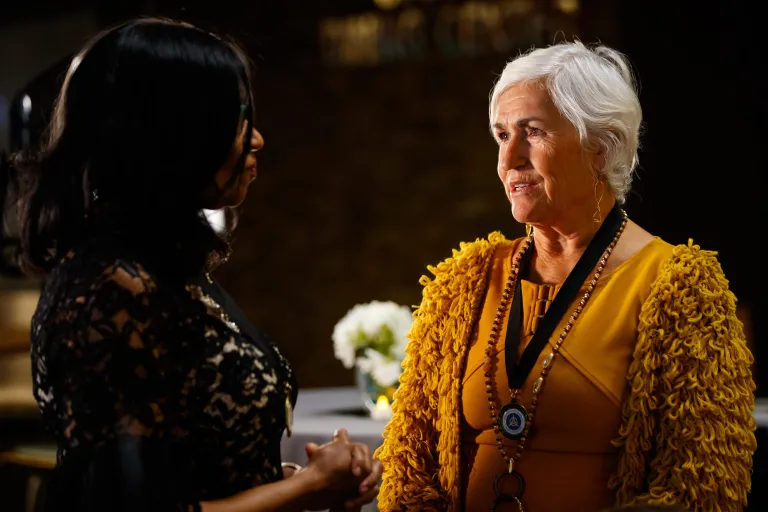 Two women conversing, one in black lace, the other in yellow cardigan with a medal.