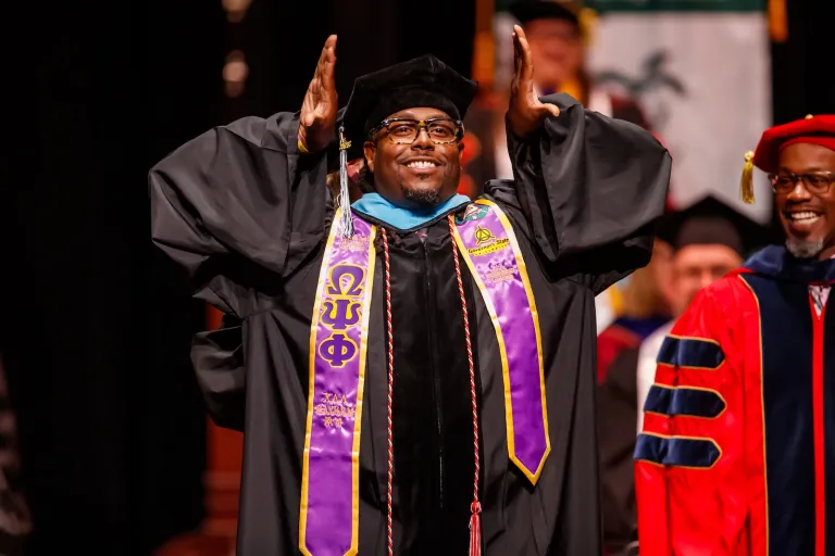 Smiling doctoral graduate raises their hands in celebration.