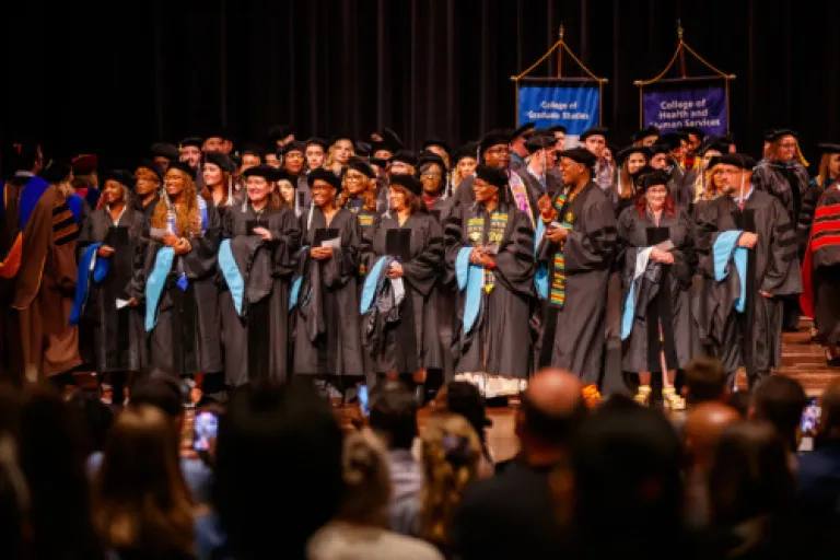 A smiling Georgia State University doctoral graduate in a blue cap and gown holds a diploma.