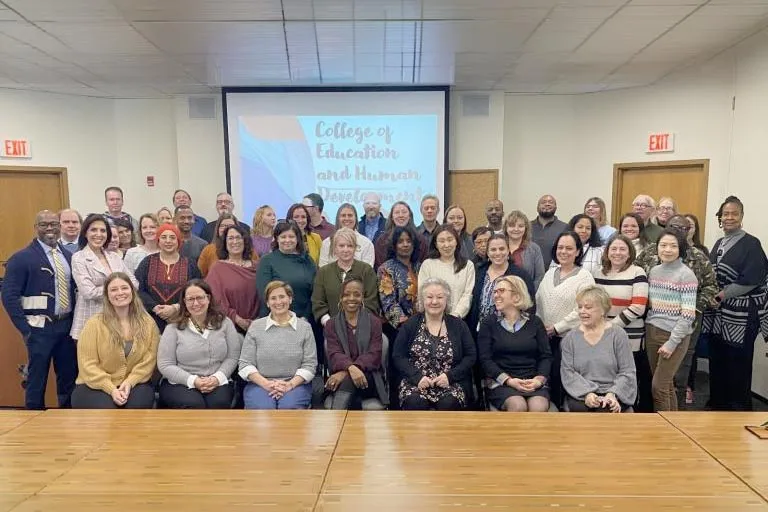 Diverse group of CEHD admins and faculty posing in a conference room with a presentation screen.