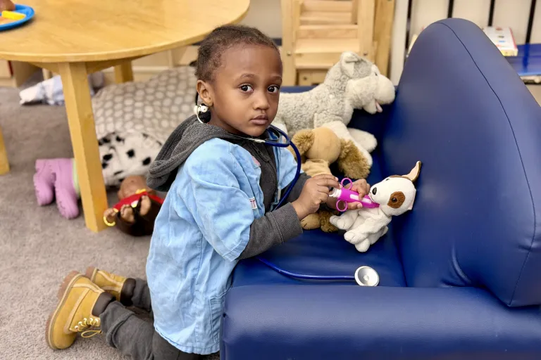 Young child in doctor smock, playing veterinarian with a stuffed dog. 