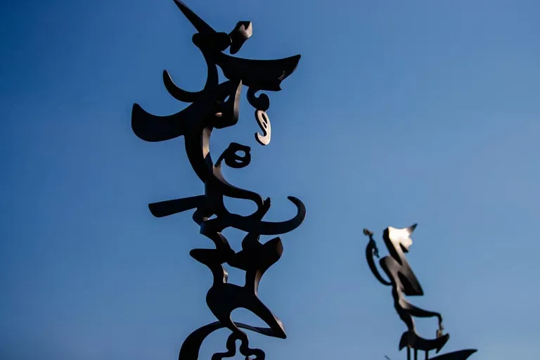 Two dark abstract metal sculptures against a clear blue sky.