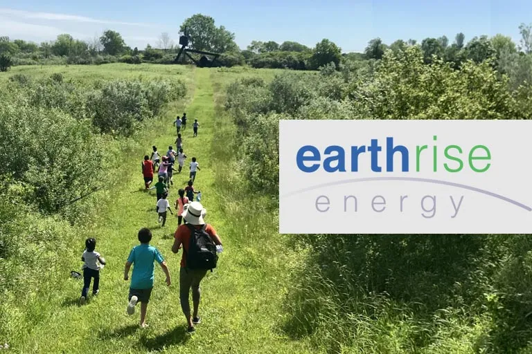 Children and adults walk on a path through a green field. Earthrise Energy logo.