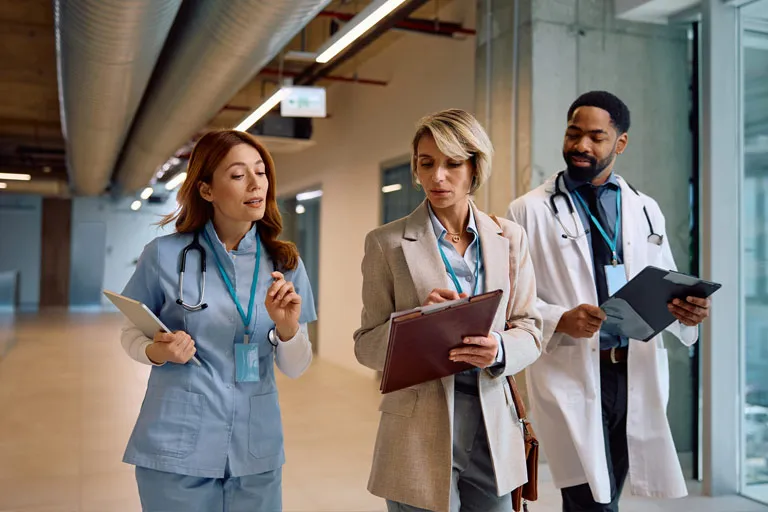Nurse, administrator, and doctor walking and conversing in a modern hospital hallway.