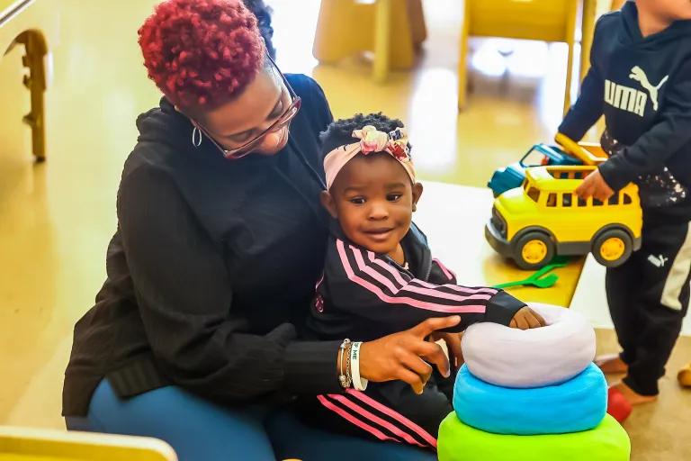 Female teacher playing a stacking game with young child. 
