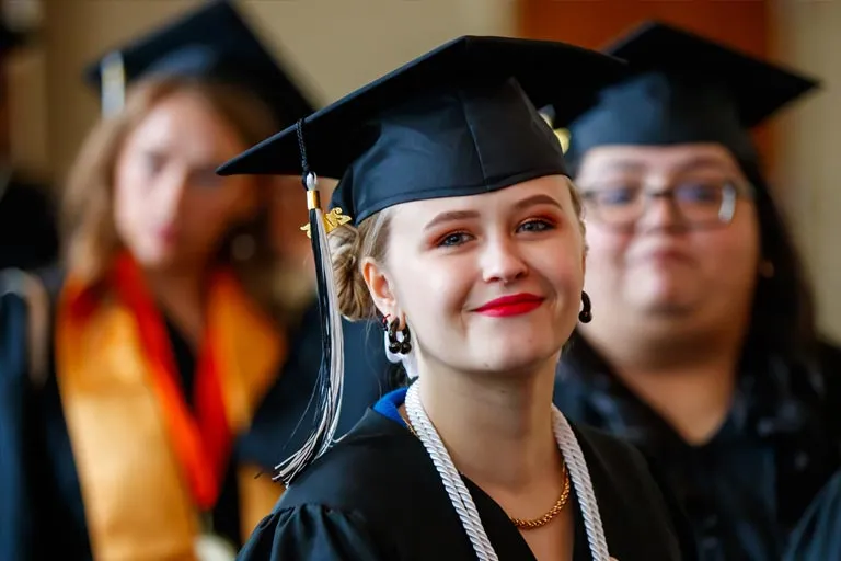 Smiling young woman in graduation cap and gown.
