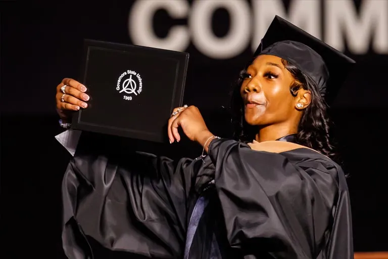Young Black woman in graduation cap and gown proudly holding her diploma.