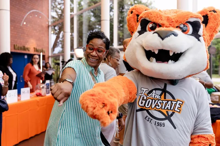 Happy woman and Jax the Jaguar mascot in "GovState" shirt giving thumbs up.