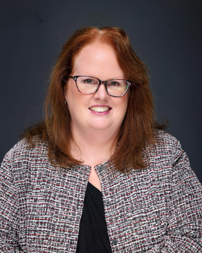 Woman with red hair, in glasses and black and white suit jacket