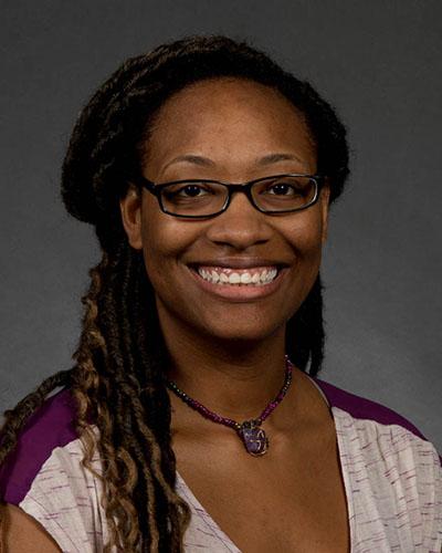 Woman in long black braids and glasses, in purple and white shirt