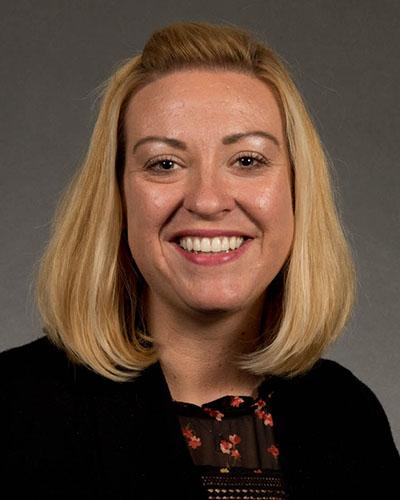 Woman in short blonde hair, in black flowered shirt and black jacket