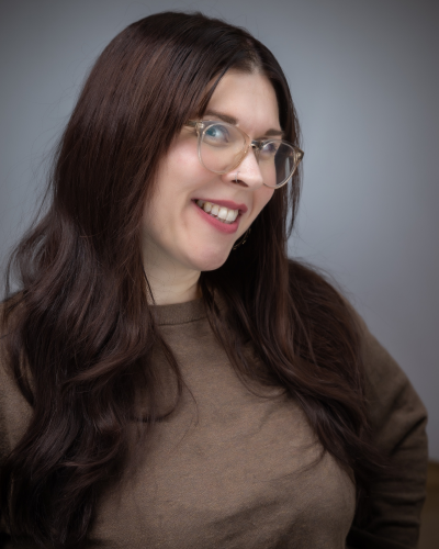 Woman with glasses and long brown hair, in brown shirt