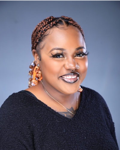 Professional headshot of woman with reddish-black braids, wearing a black sweater