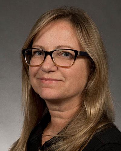 Professional headshot of woman with long blond hair, wearing glasses and dark shirt