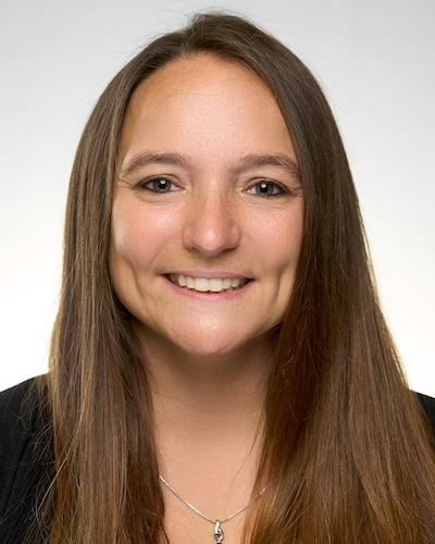 Professional headshot of woman with long brown hair, wearing black shirt