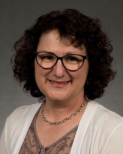 Professional headshot of woman with short curly hair, wearing glasses and white sweater