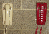 Beige wall phone next to a red emergency phone on a textured wall.