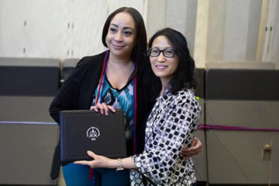 Two women smiling, one holding a certificate, the other with an arm around her.