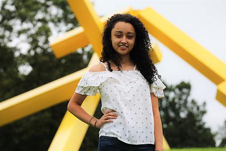 Lluvia standing near a bright yellow abstract sculpture.