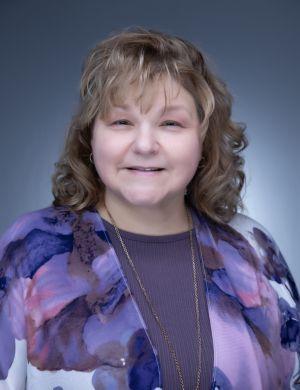 Smiling woman with light brown hair in a purple floral cardigan.