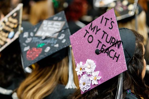 Graduate wearing a decorated cap that reads, "It's my turn to teach."
