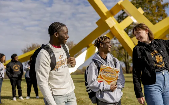 Group of students walking and talking outside by an abstract sculpture