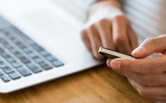 Person holding phone in front of laptop