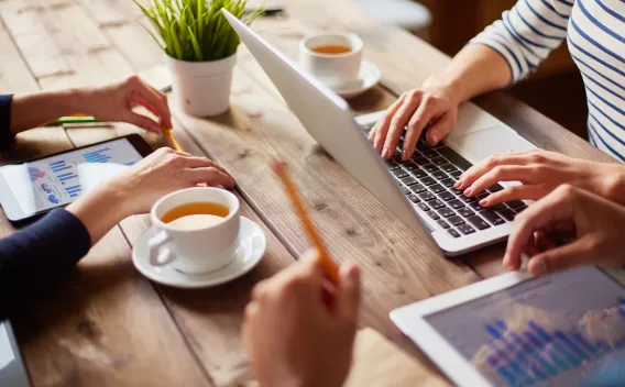 3 sets of hands at a table working on tablets and a laptop