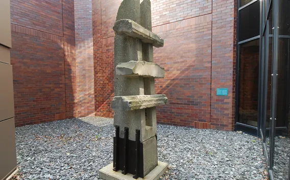 Abstract concrete sculpture with stacked organic forms, next to brick and glass walls.