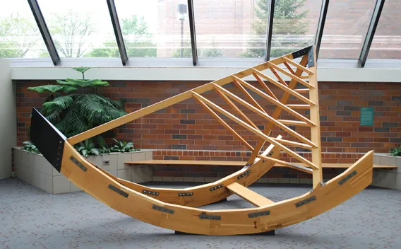 Light wooden sculpture with a curved base and truss-like top in a bright atrium.