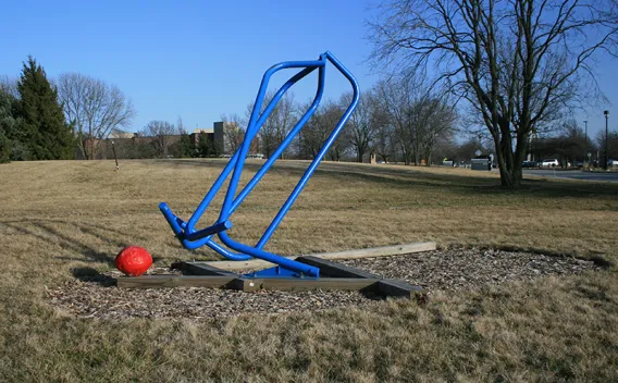 Blue playground equipment and a red ball on dry grass under a clear blue sky.