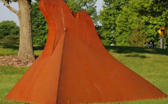 Rust-colored abstract sculpture with a wavy form on green grass.