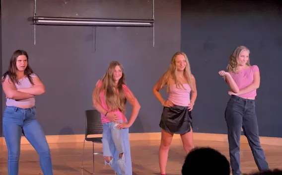 Four young women in pink tops posing on a stage during a performance.