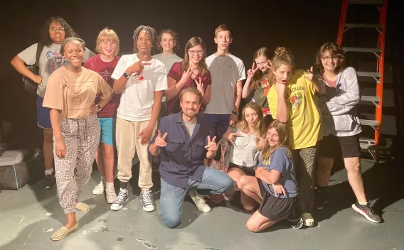 Group of diverse teens and an adult posing with peace signs in a theater.