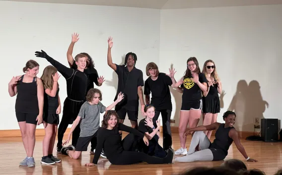 Group of young people in black clothing posing and gesturing on a stage.