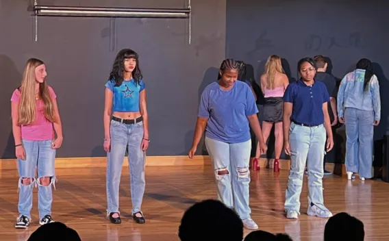 Four casually dressed young people on a stage, others in the blurred background.
