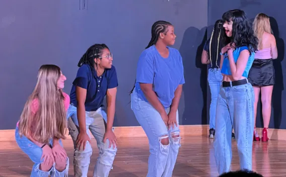 Four young people on stage, two talking expressively, two watching intently.