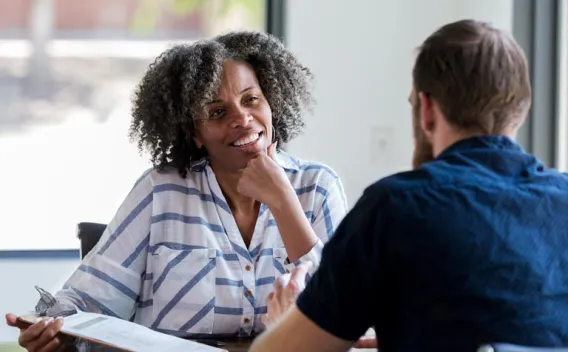 Smiling woman with gray curly hair talks to a man, holding a clipboard.