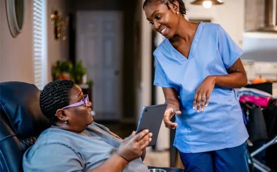 Caregiver and client smiling while looking at a tablet.