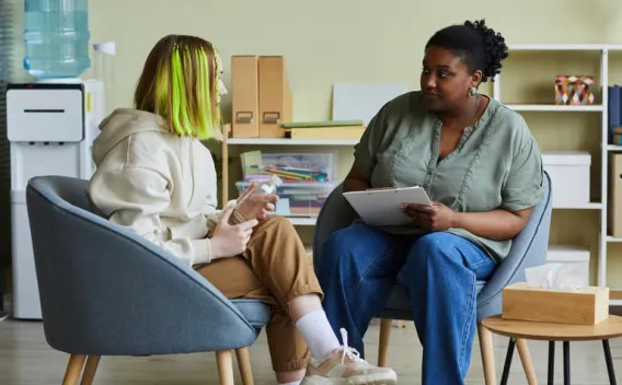 Woman with green hair talks to a counselor holding a clipboard.