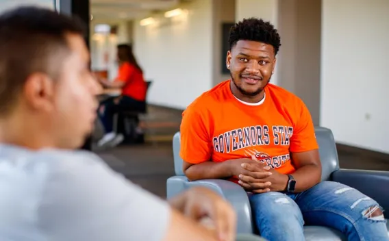 Students sitting in chairs and talking in a hallway
