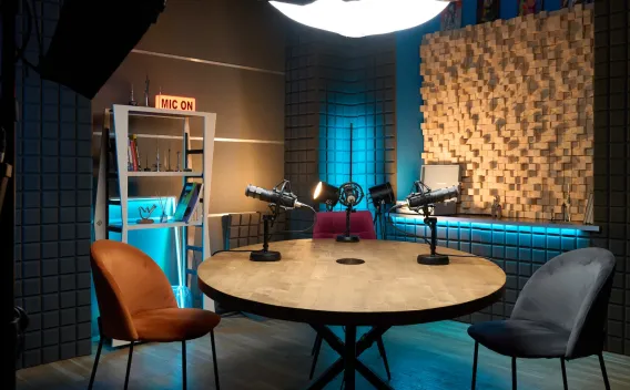 Professional podcast studio with round table, three mics, chairs, and acoustic panels.