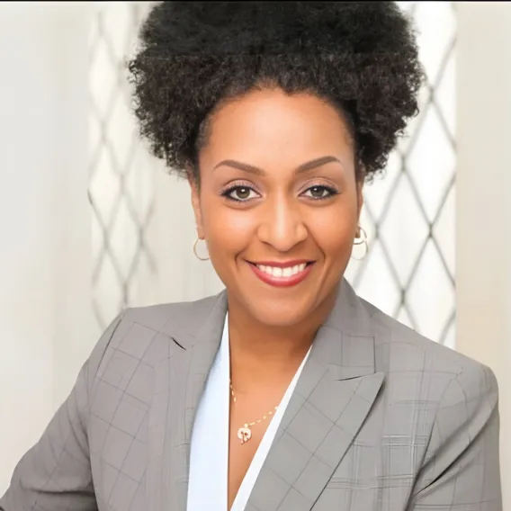  Person wearing a light gray plaid blazer and a light-colored top, posed in front of a window with a geometric patterned frame